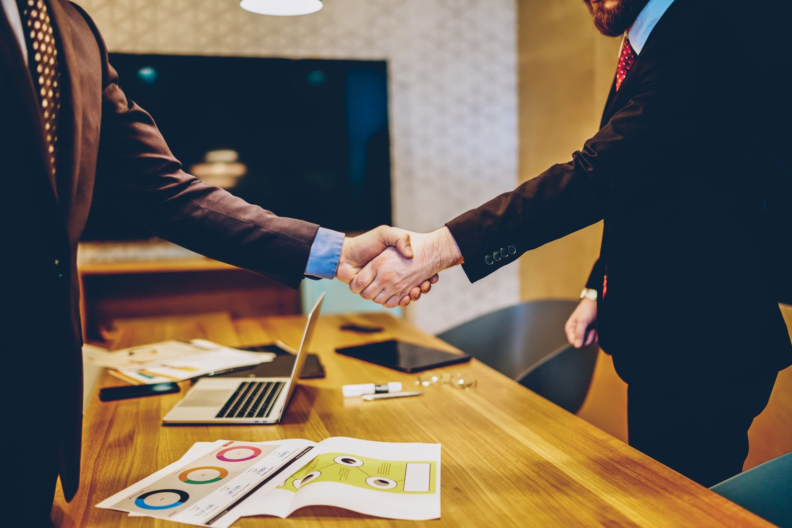 Cropped image of men in suits shaking hands making deal of sponsorship in business corporation, male entrepreneurs agree in partnership cooperation and contract during formal meeting in office